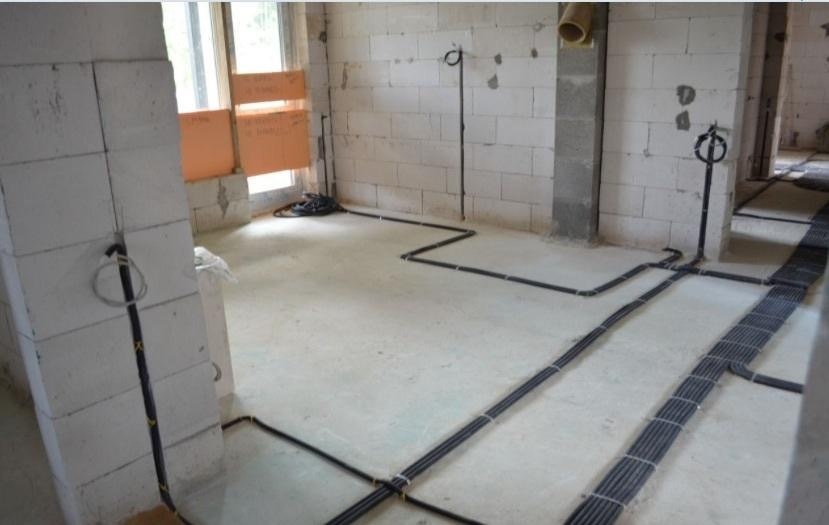 Surowy stan: czarne przewody elektryczne ułożone na podłodze i ścianach z bloków betonu komórkowego, widoczne puszki instalacyjne i okablowanie przy oknie.