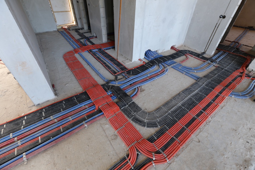 Rozłożone kable elektryczne w peszlach (czerwone, niebieskie, czarne) na podłodze w surowym stanie, mocowane klamrami w Warszawie. Widok z góry na instalację.