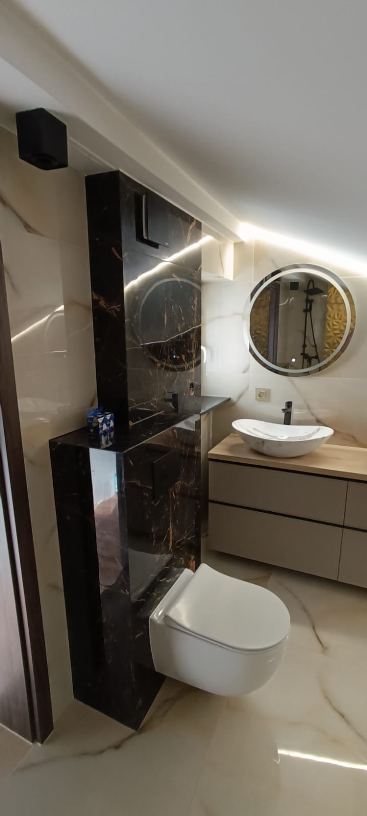 Nowoczesna łazienka w beżach i czerni. Umywalka nablatowa, podświetlane lustro, toaleta podwieszana i marmurowe wykończenia tworzą elegancką całość.