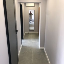 Bogacz-Studziński - Wykończony korytarz w szarościach z lustrem, w którym odbija się osoba robiąca zdjęcie. Nowe płytki na podłodze, świeżo pomalowane ściany i nowe drzwi.