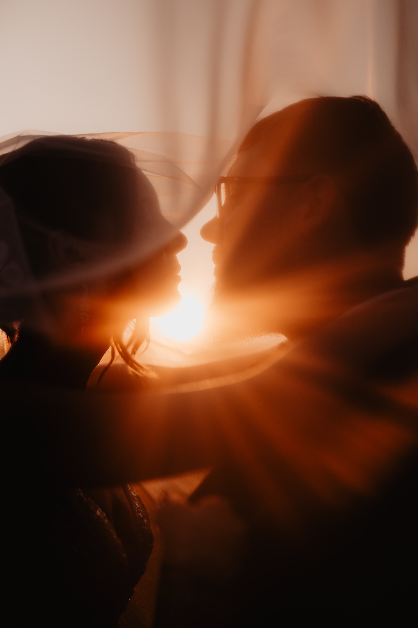 Silhouetted para młoda w kontraście ze słońcem, panna młoda w welonie, delikatne rozmycie, ciepłe barwy zachodu słońca.