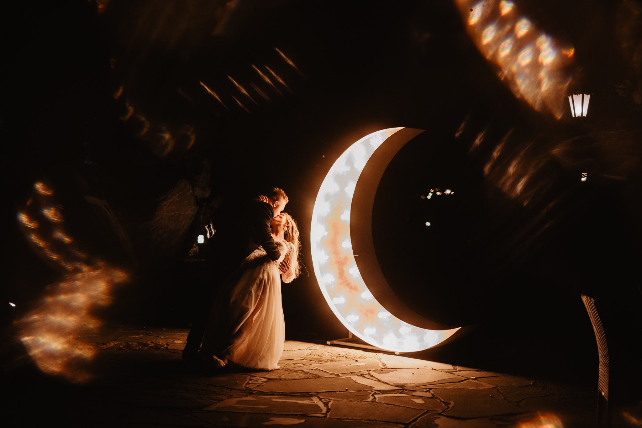 Para młoda w objęciach na tle podświetlanego księżyca. Romantyczna sceneria z efektem świetlnym i kamienną posadzką.