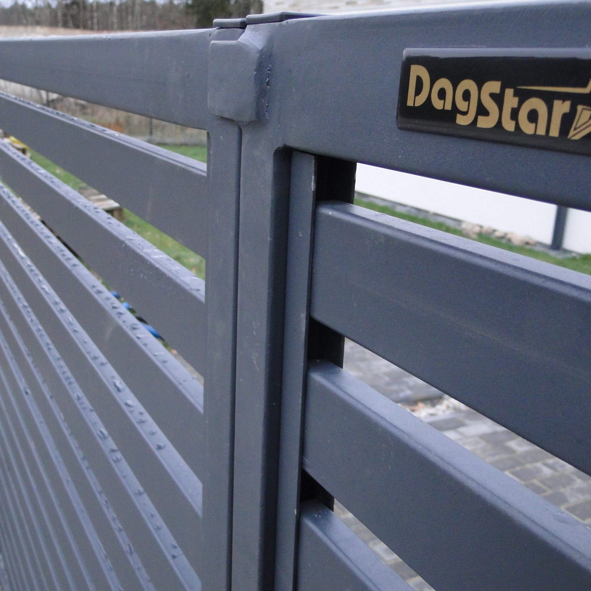 Szczegółowe ujęcie szarego, metalowego ogrodzenia panelowego z logo Dagstar, ukazujące solidne łączenia i precyzję wykonania.