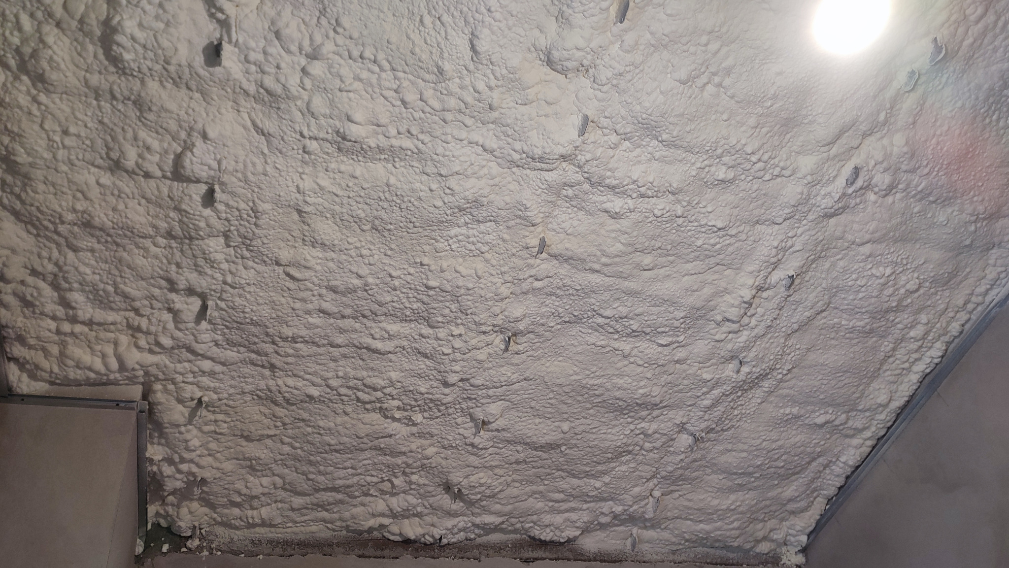 Poddasze po ociepleniu pianą PUR otwartokomórkową, widoczne metalowe profile konstrukcyjne. Biała, nierówna powierzchnia piany z widocznymi otworami montażowymi.