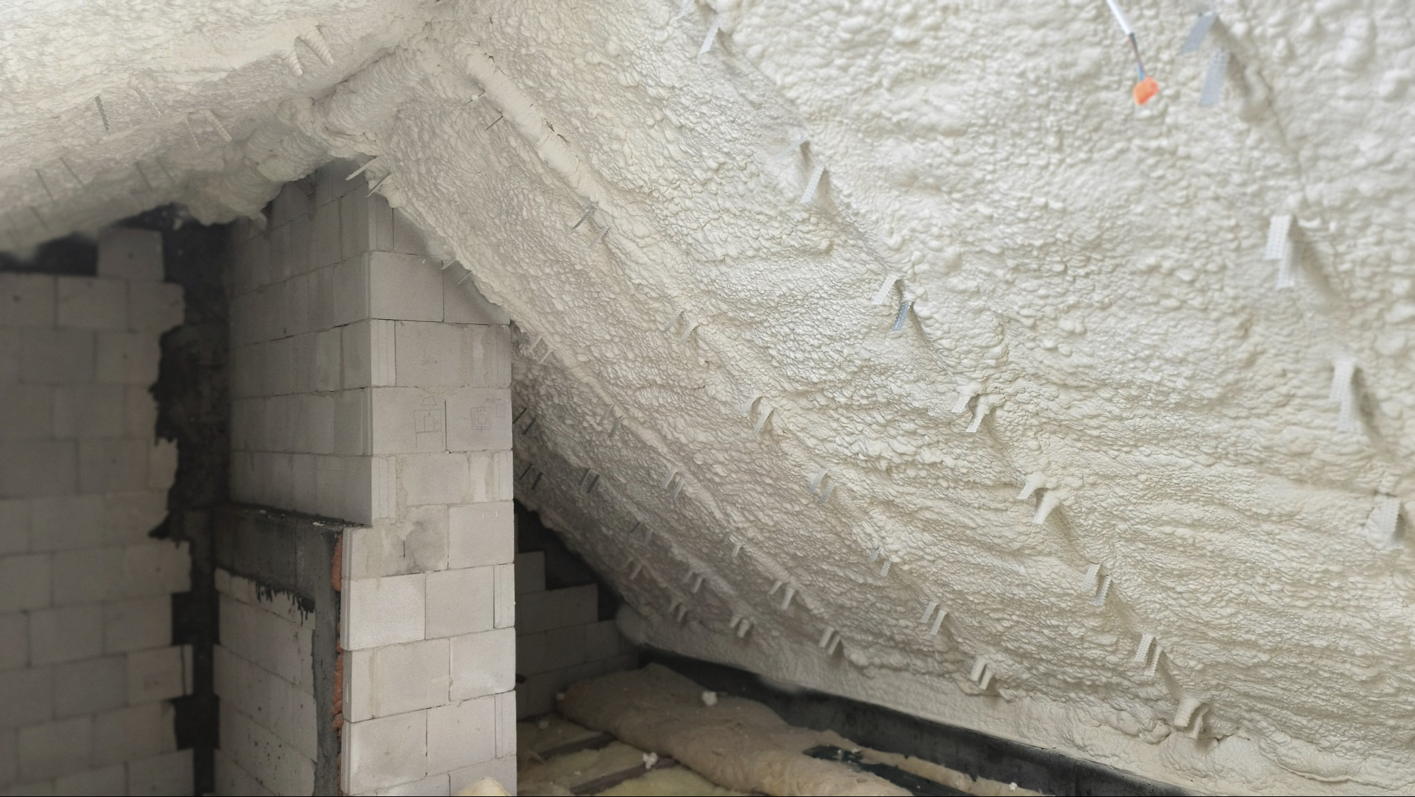 Poddasze po ociepleniu pianą PUR otwartokomórkową SmartPur, widoczne bloki betonowe i wystające uchwyty montażowe w pianie. Detal realizacji ocieplenia.