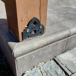 RAFAŁ GAJEWSKI - Metalowa stopa słupa drewnianego wspawana i pomalowana, podtrzymująca konstrukcję nad szarymi płytkami tarasowymi z zaokrąglonymi krawędziami. Detal wykonany na zamówienie.