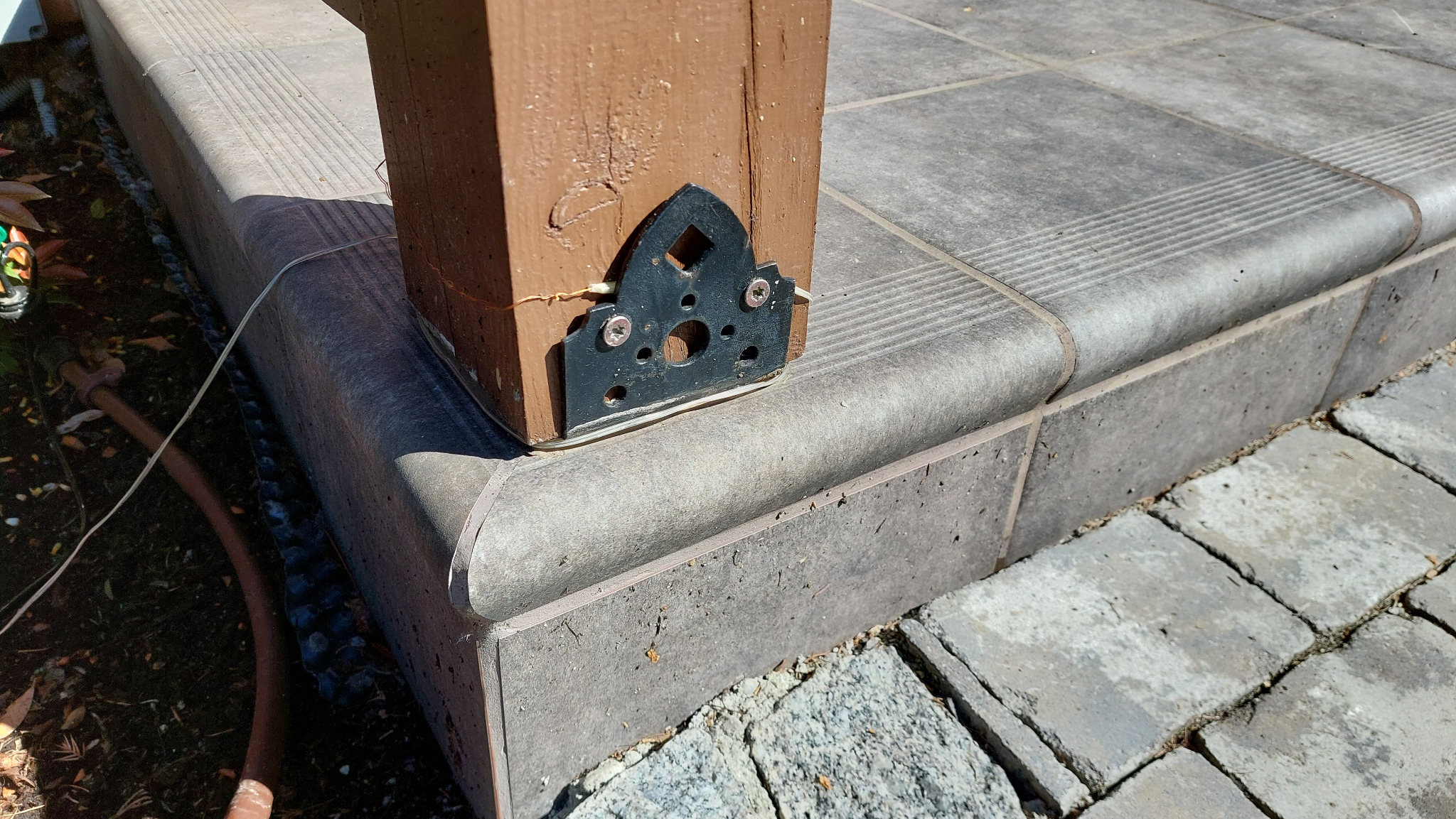 Metalowa stopa słupa drewnianego wspawana i pomalowana, podtrzymująca konstrukcję nad szarymi płytkami tarasowymi z zaokrąglonymi krawędziami. Detal wykonany na zamówienie.