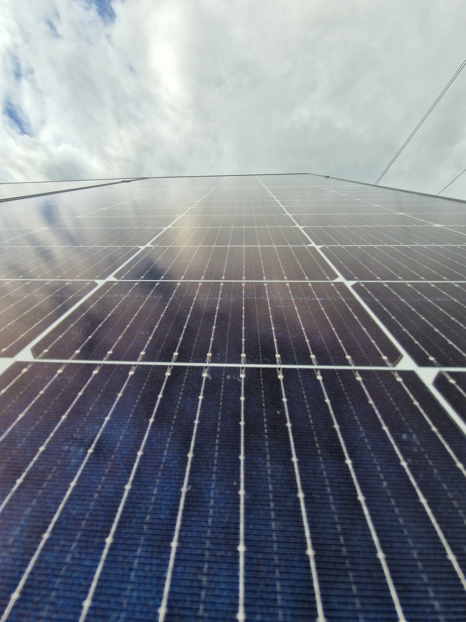 Nisko kątowe ujęcie paneli słonecznych z widocznym niebem. Układ paneli tworzy geometryczny wzór, podkreślony przez światło odbijające się od powierzchni.