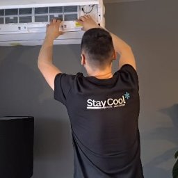 Stay Cool - Serwisant w Kraśniku czyści filtry klimatyzacji ściennej w pomieszczeniu o szarych ścianach. Mężczyzna w koszulce z logo firmy Stay Cool.