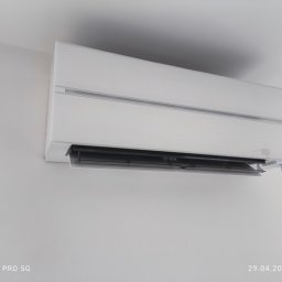 Stay Cool - Biała klimatyzacja ścienna zamontowana w jasnym pomieszczeniu. Widoczny detal w postaci otwartej klapy wylotowej powietrza. Minimalistyczny design.