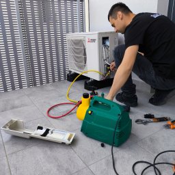 Stay Cool - Serwisant w trakcie montażu klimatyzacji Mitsubishi Electric na balkonie, używając specjalistycznych narzędzi i pompy próżniowej. Widoczne przewody i elementy instalacji.
