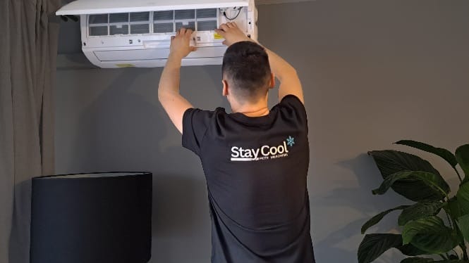 Serwisant w Kraśniku czyści filtry klimatyzacji ściennej w pomieszczeniu o szarych ścianach. Mężczyzna w koszulce z logo firmy Stay Cool.