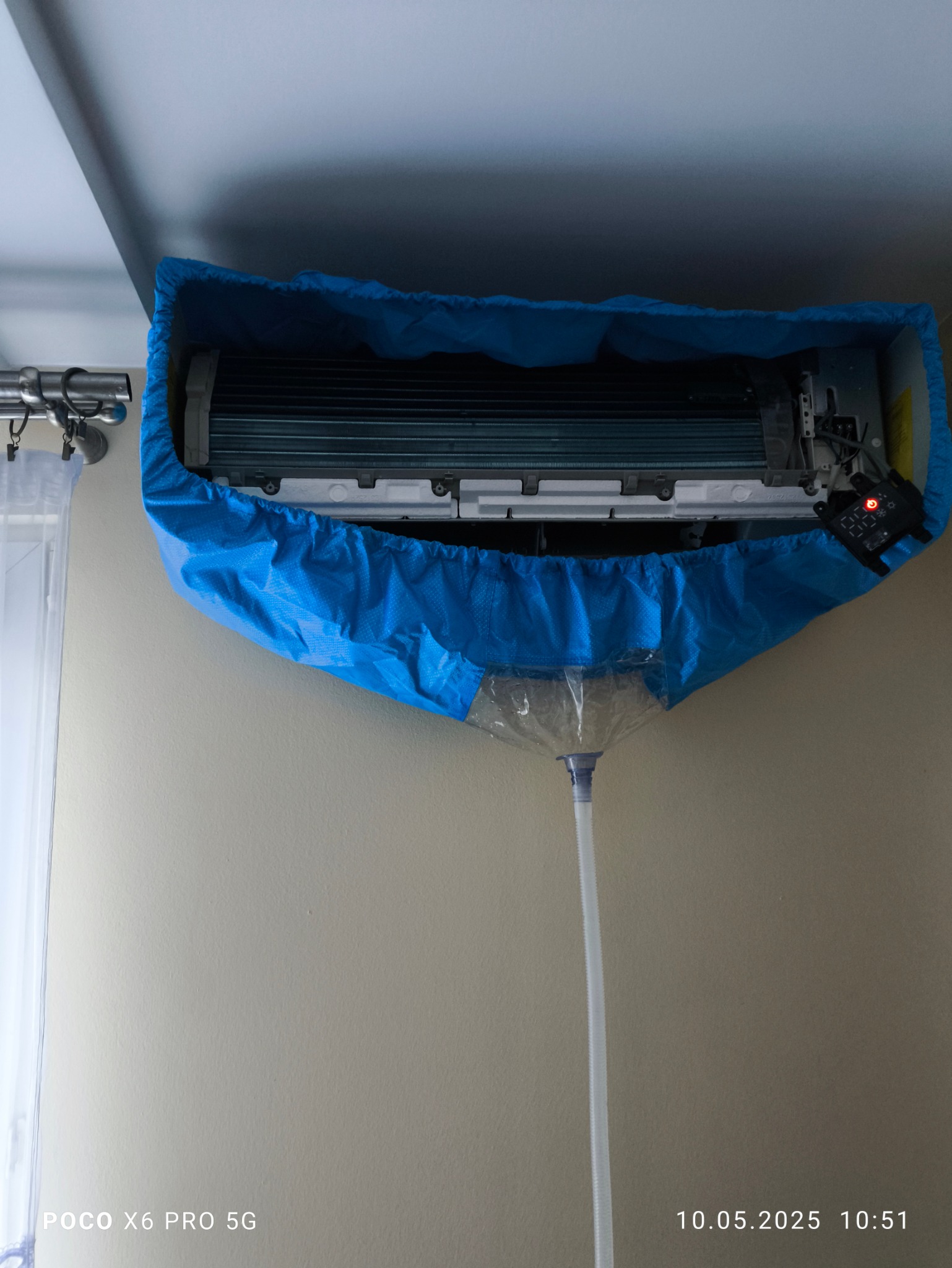 Czyszczenie klimatyzacji ściennej za pomocą specjalnego pokrowca i węża odprowadzającego wodę, widoczne żebra chłodnicy.