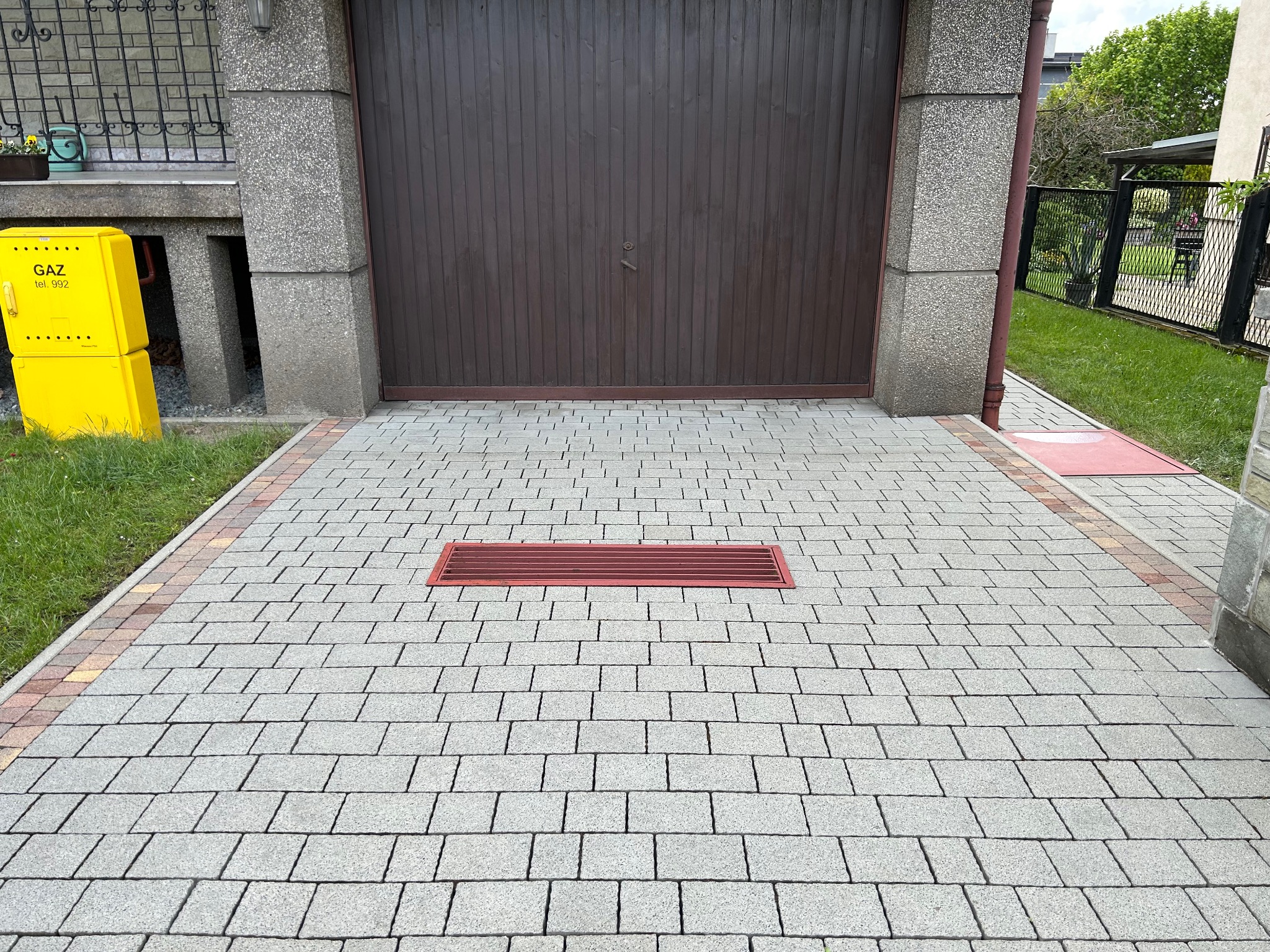 Ułożona kostka brukowa przed garażem w Mysłowicach, z widoczną kratką odpływową i żółtą skrzynką gazową. Czysta powierzchnia, równy wzór.