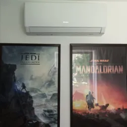 Biała klimatyzacja marki Gree zamontowana na ścianie, pod nią dwa plakaty Star Wars: Jedi Fallen Order i Mandalorian, tworząc nowoczesną aranżację wnętrza.