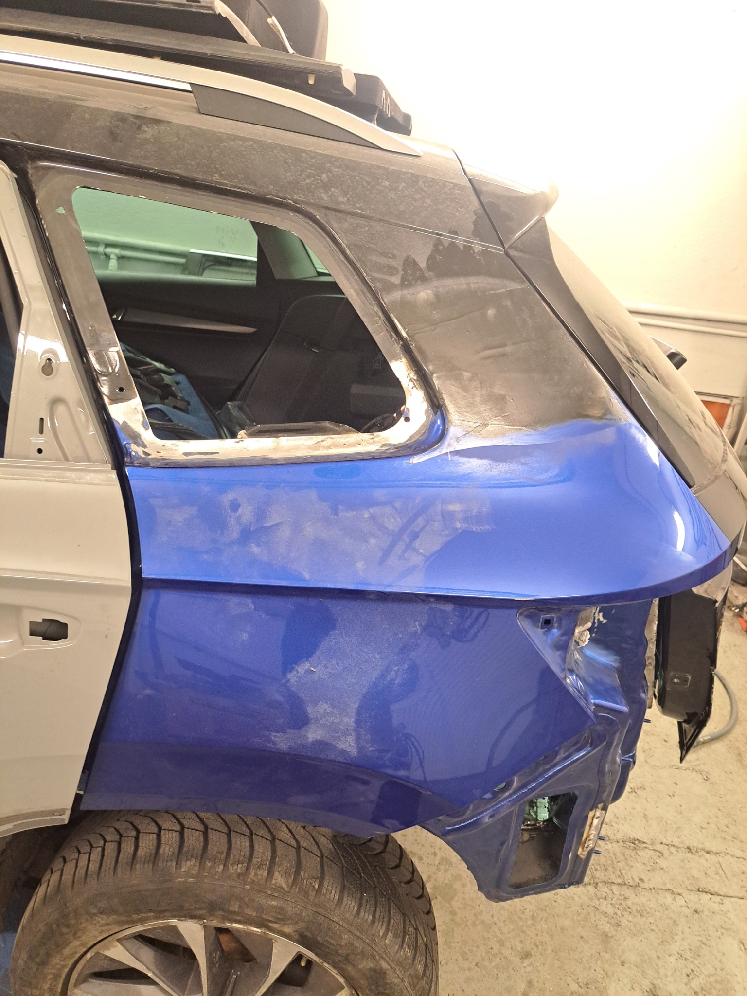 Fragment nadwozia samochodu kombi w trakcie naprawy blacharskiej, z widocznymi śladami szpachlowania i częściowo nałożonym lakierem w kolorze niebieskim.