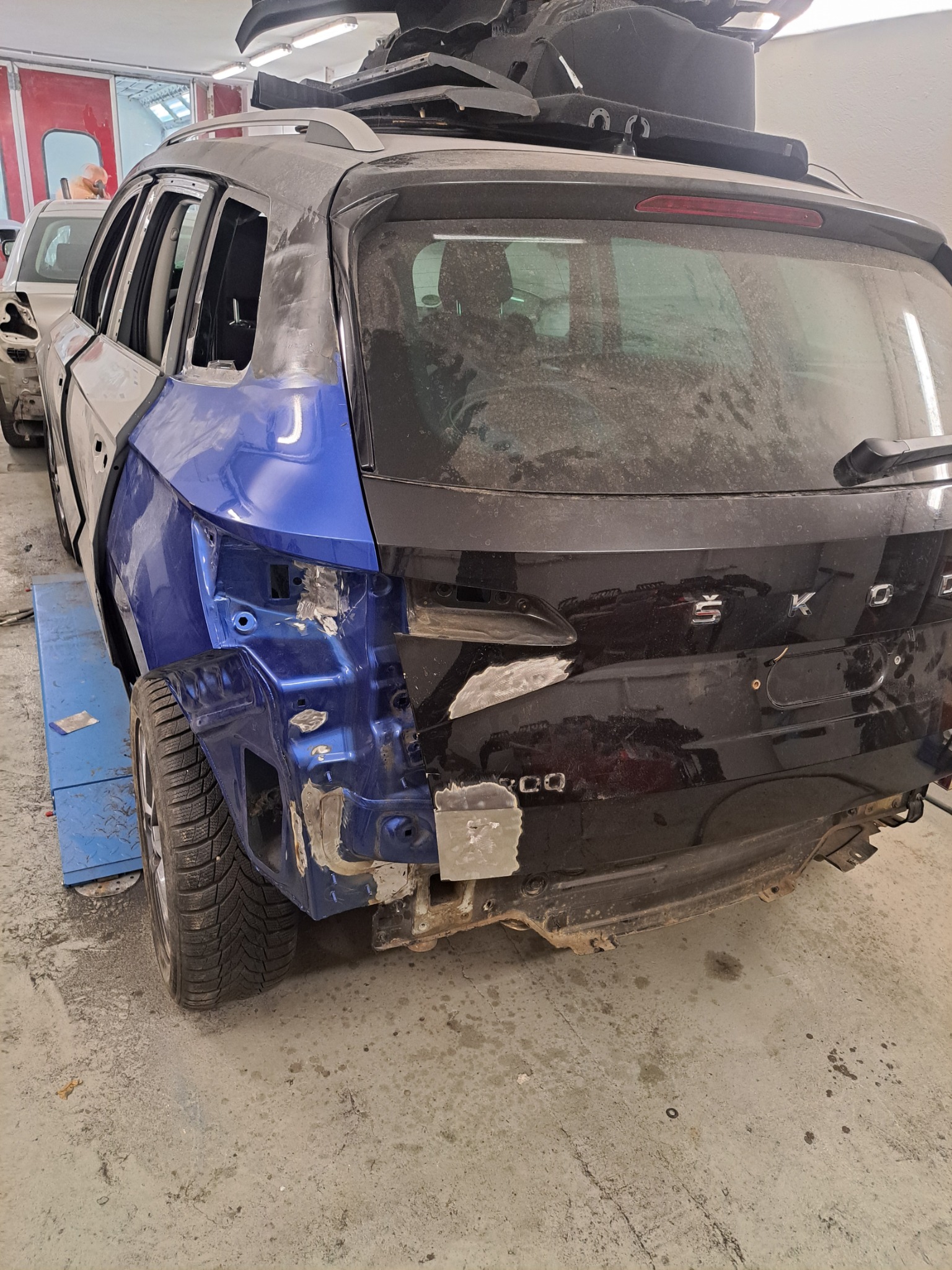 Częściowo naprawiony, niebiesko-czarny samochód Skoda w warsztacie, widok z tyłu. Blacha i szpachla na karoserii, przygotowanie do lakierowania.