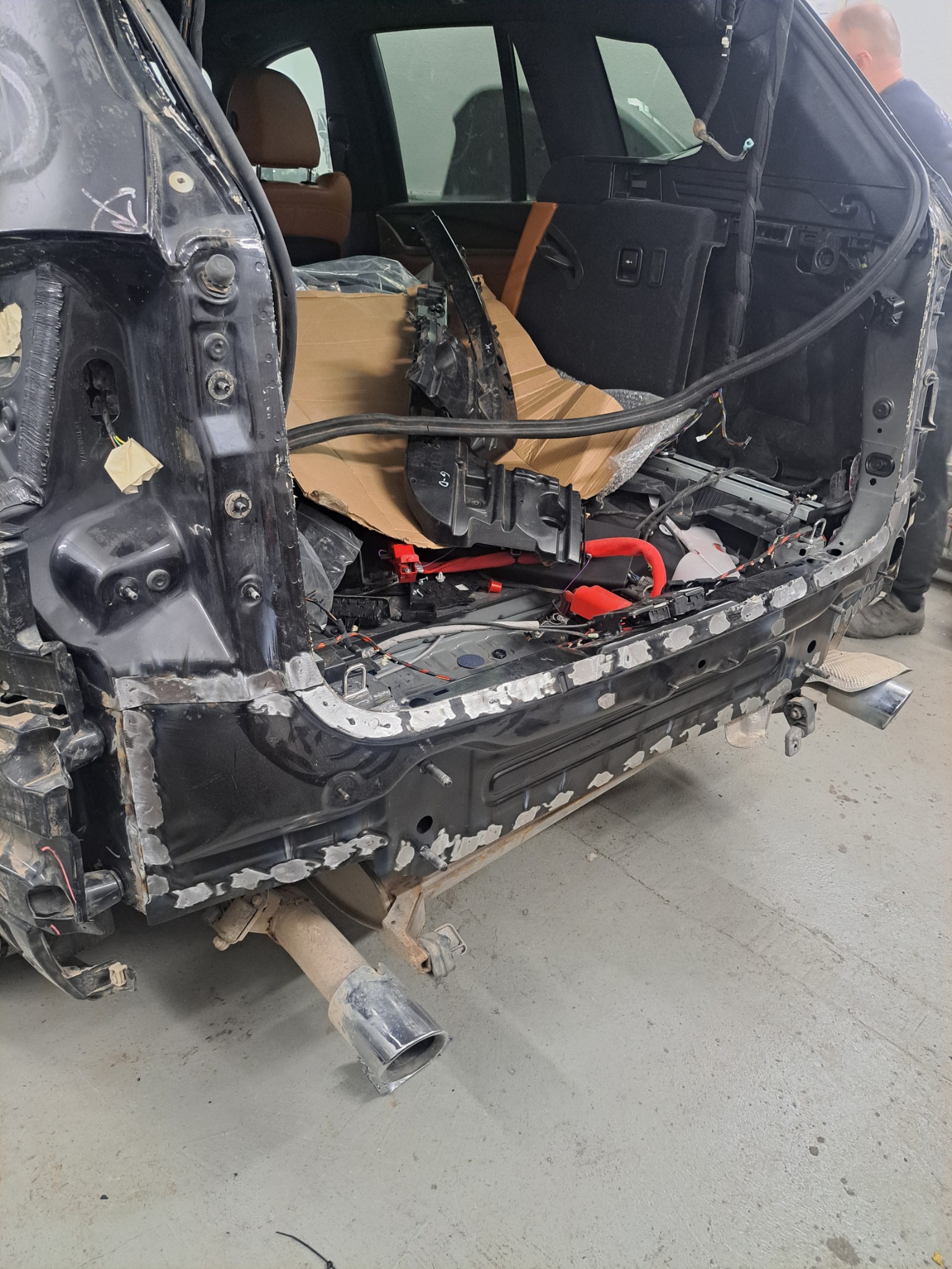 Czarne auto po wypadku w trakcie naprawy blacharskiej. Widoczne elementy konstrukcyjne, spawane fragmenty karoserii i fragment układu wydechowego.