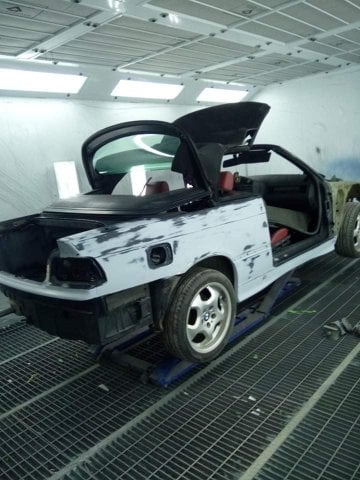 Przygotowany do lakierowania kabriolet BMW E36 na podnośniku w lakierni. Widoczne szpachlowane elementy karoserii i otwarty dach. Metalowa podłoga lakierni.