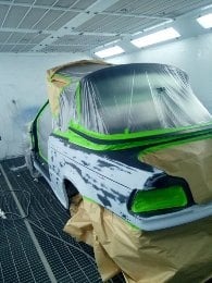 Samochód w komorze lakierniczej, przygotowany do lakierowania. Częściowo zamaskowany folią i papierem, widoczne ślady szpachli.