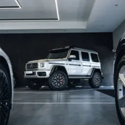 Biały samochód terenowy z czarnymi akcentami i czerwonymi zaciskami hamulcowymi, zaparkowany w nowoczesnym salonie samochodowym z oświetleniem LED.