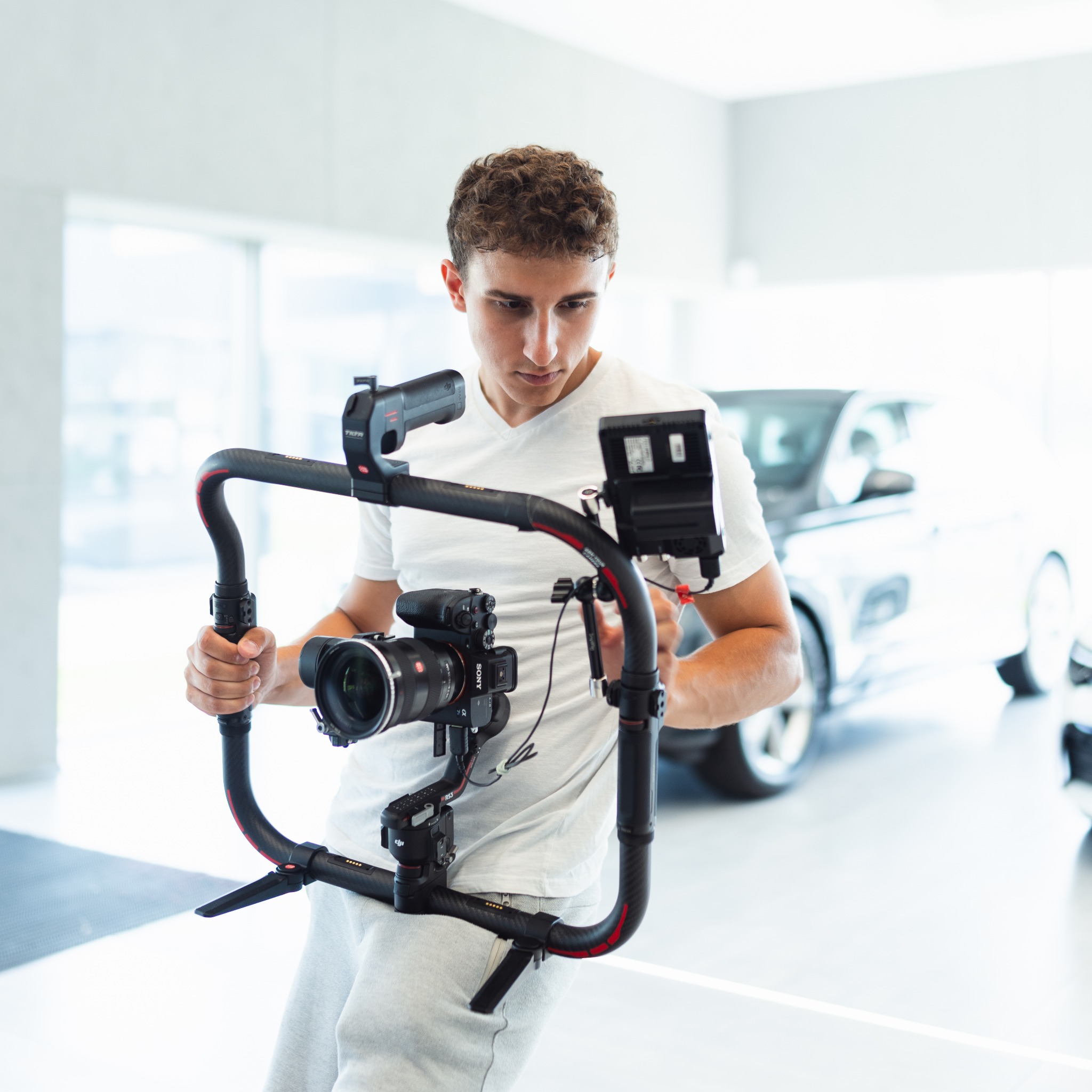Operator z kamerą Sony i stabilizatorem DJI Ronin-RS3 w salonie samochodowym, przygotowujący się do nagrania materiału wideo z nowym modelem auta.