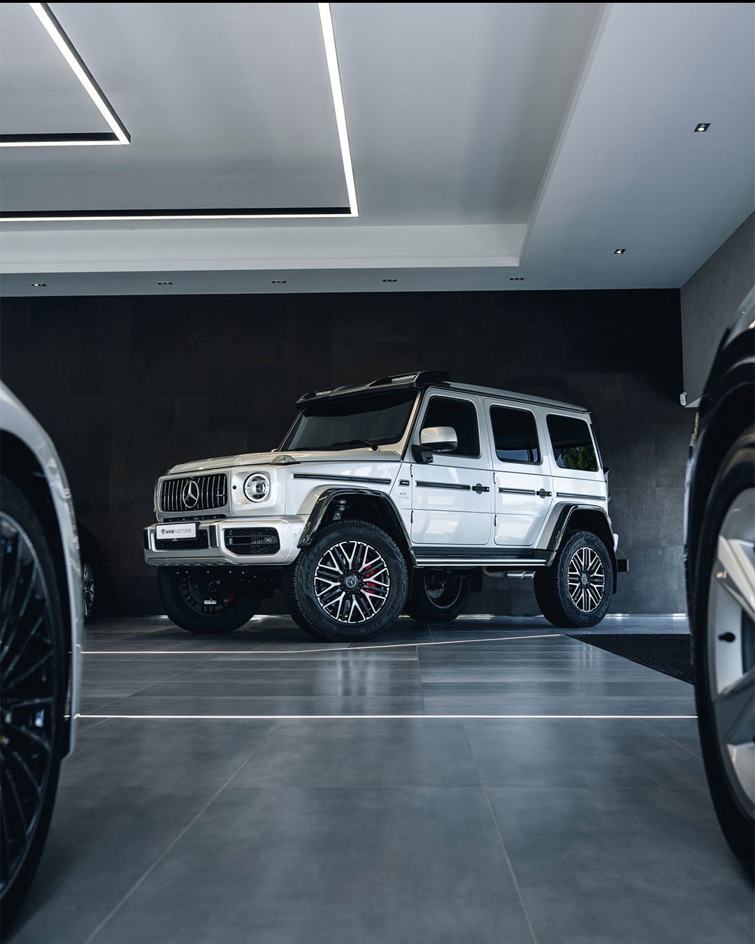 Biały samochód terenowy z czarnymi akcentami i czerwonymi zaciskami hamulcowymi, zaparkowany w nowoczesnym salonie samochodowym z oświetleniem LED.