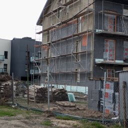 Lewon - Budynek wielorodzinny w trakcie ocieplania, widoczne rusztowania i materiały izolacyjne. Częściowo otynkowana elewacja, okna zabezpieczone folią.