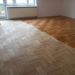 Lewon - Parkiet w jodełkę częściowo polakierowany. Widoczny fragment osoby lakierującej podłogę i wiadro z lakierem. Okno i grzejnik w tle. Podłoga w trakcie renowacji.