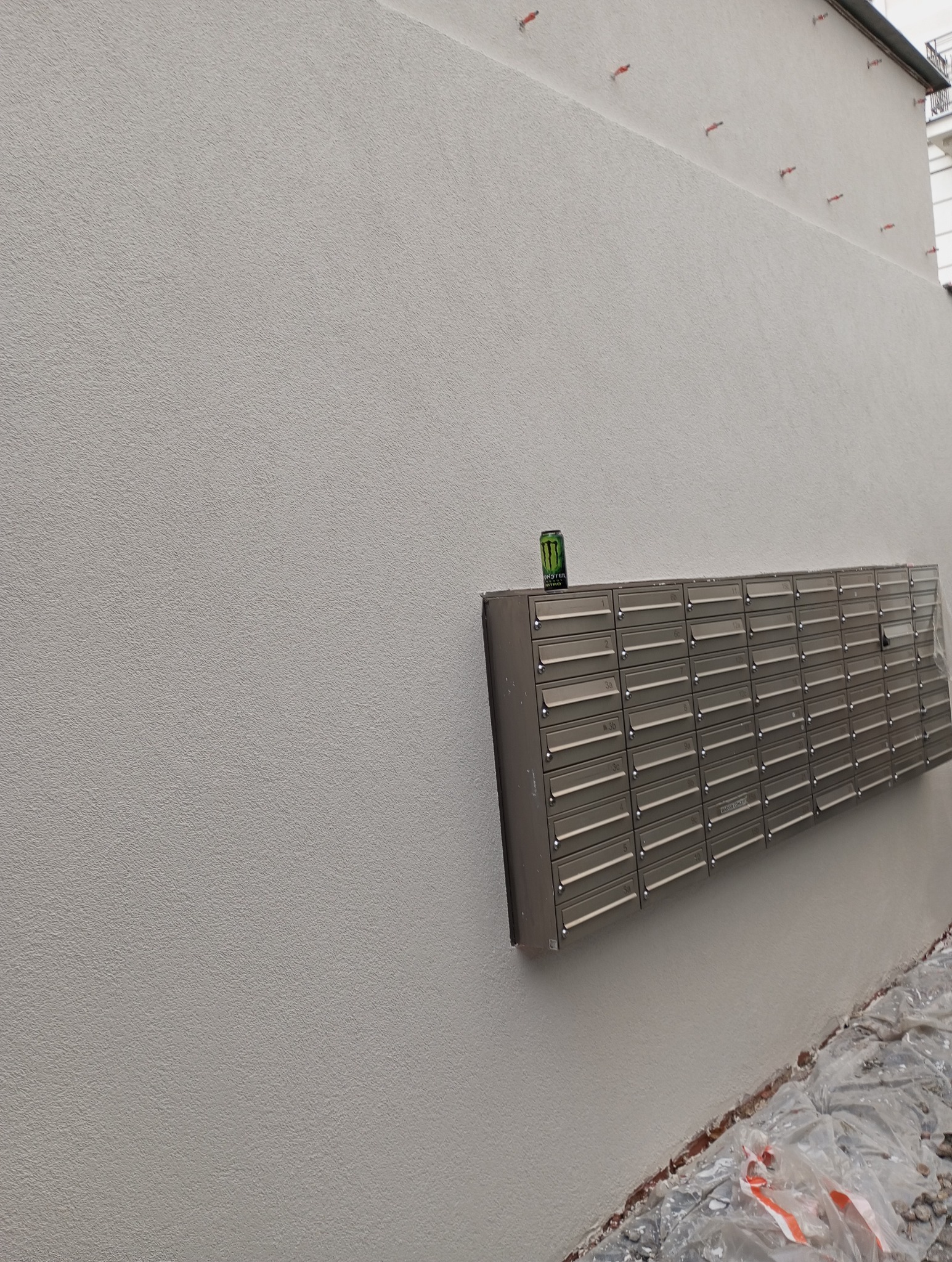 Ściana budynku po tynkowaniu z puszką napoju na skrzynkach pocztowych. Widoczne ślady po pracach wykończeniowych przy gruncie.