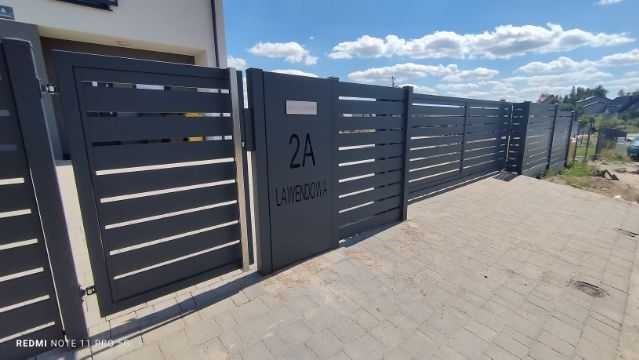 Nowoczesna, grafitowa brama wjazdowa z poziomymi panelami i numerem domu 2A 'Lawendowa', dopasowana do ogrodzenia w tym samym stylu. Brukowana ścieżka.