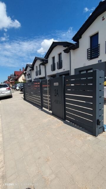 Nowoczesna, przesuwna brama wjazdowa w kolorze grafitowym z adresem 2A, zamontowana przed szeregiem domów jednorodzinnych w słoneczny dzień.