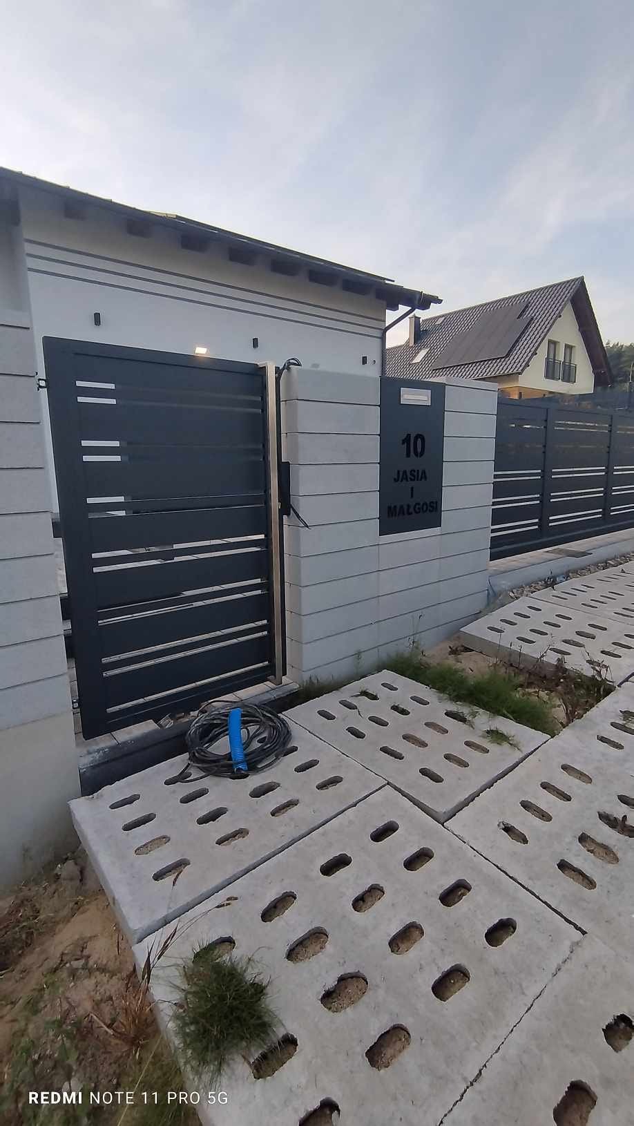 Nowoczesna, grafitowa brama wjazdowa z poziomymi panelami, wkomponowana w ogrodzenie z betonowych bloczków z numerem posesji '10 u Jasia i Małgosi'.