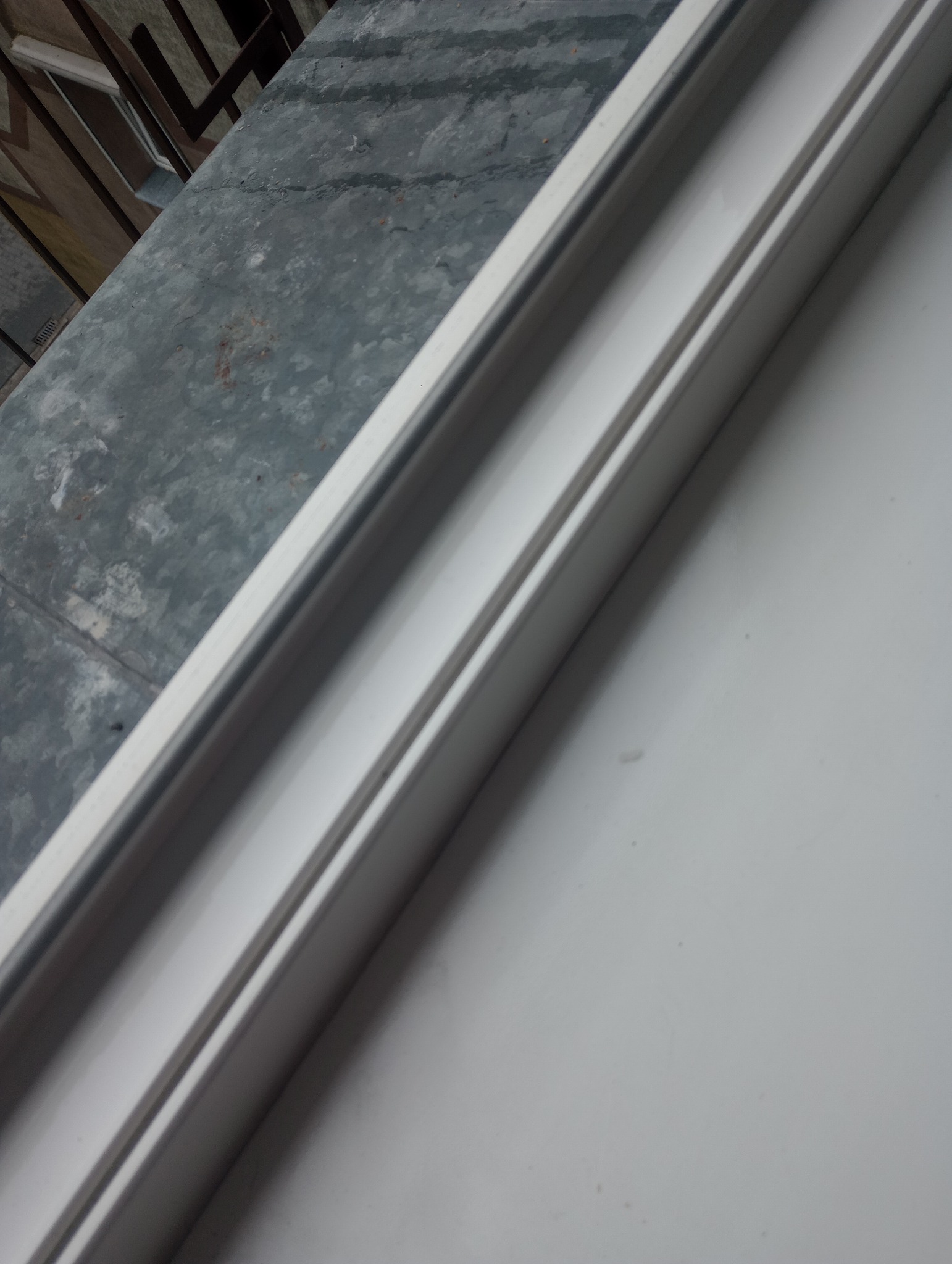 Biała rama okienna z widocznym brudnym parapetem, ujęcie pod kątem. Detal okna po remoncie, wymagający czyszczenia.