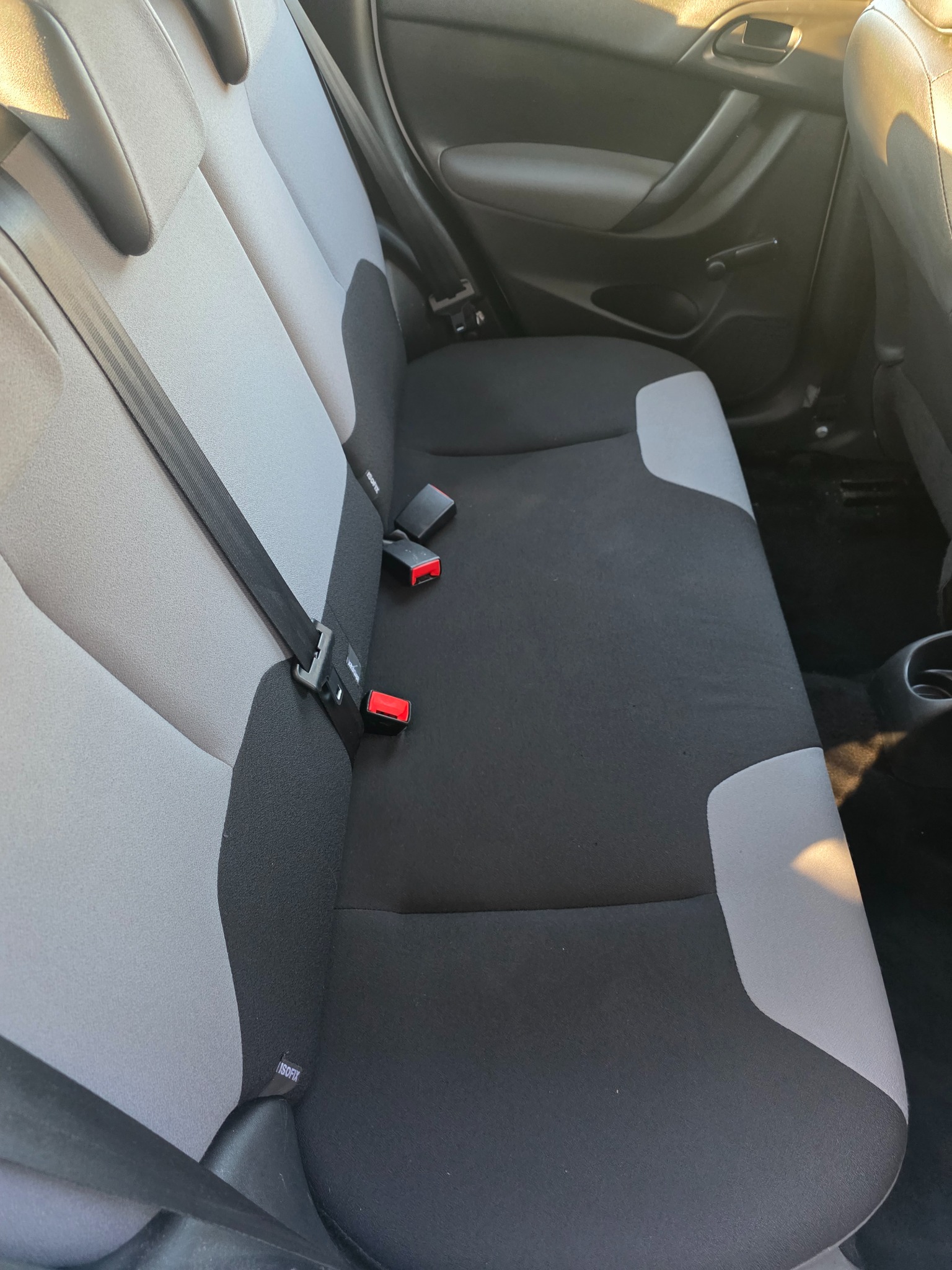 Szare i czarne siedzenie samochodu z widocznymi pasami bezpieczeństwa i mocowaniem ISOFIX, ukazujące detale tapicerki i wnętrza pojazdu.