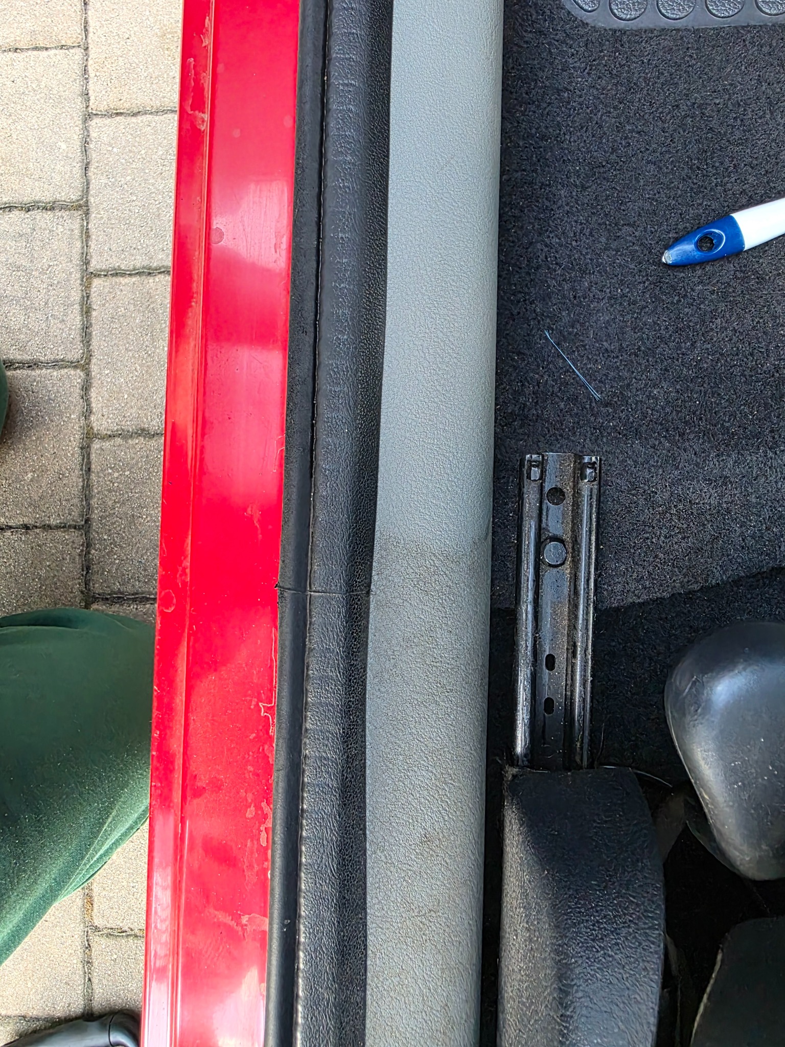 Fragment wnętrza samochodu z widoczną szczotką do czyszczenia tapicerki, sugerujący proces prania dywaników samochodowych z bliska.