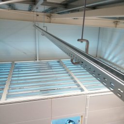 Elektro IT Sp.z.o.o - Metalowa konstrukcja podwieszona do sufitu, prawdopodobnie koryto kablowe lub element instalacji. Widoczne mocowania i perforowane profile.