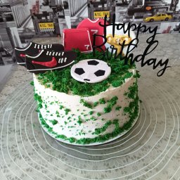 Młyn catering - Tort urodzinowy z motywem piłkarskim: zielona posypka imituje trawę, dekoracje z butów, koszulki i piłki. Napis 'Happy Birthday'. Idealny dla fana sportu.