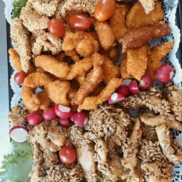 Dekoracyjna taca z różnorodnymi przekąskami: kurczak w sezamie, frytki z kurczaka i warzywa (pomidorki cherry, rzodkiewki). Idealne na przyjęcie.