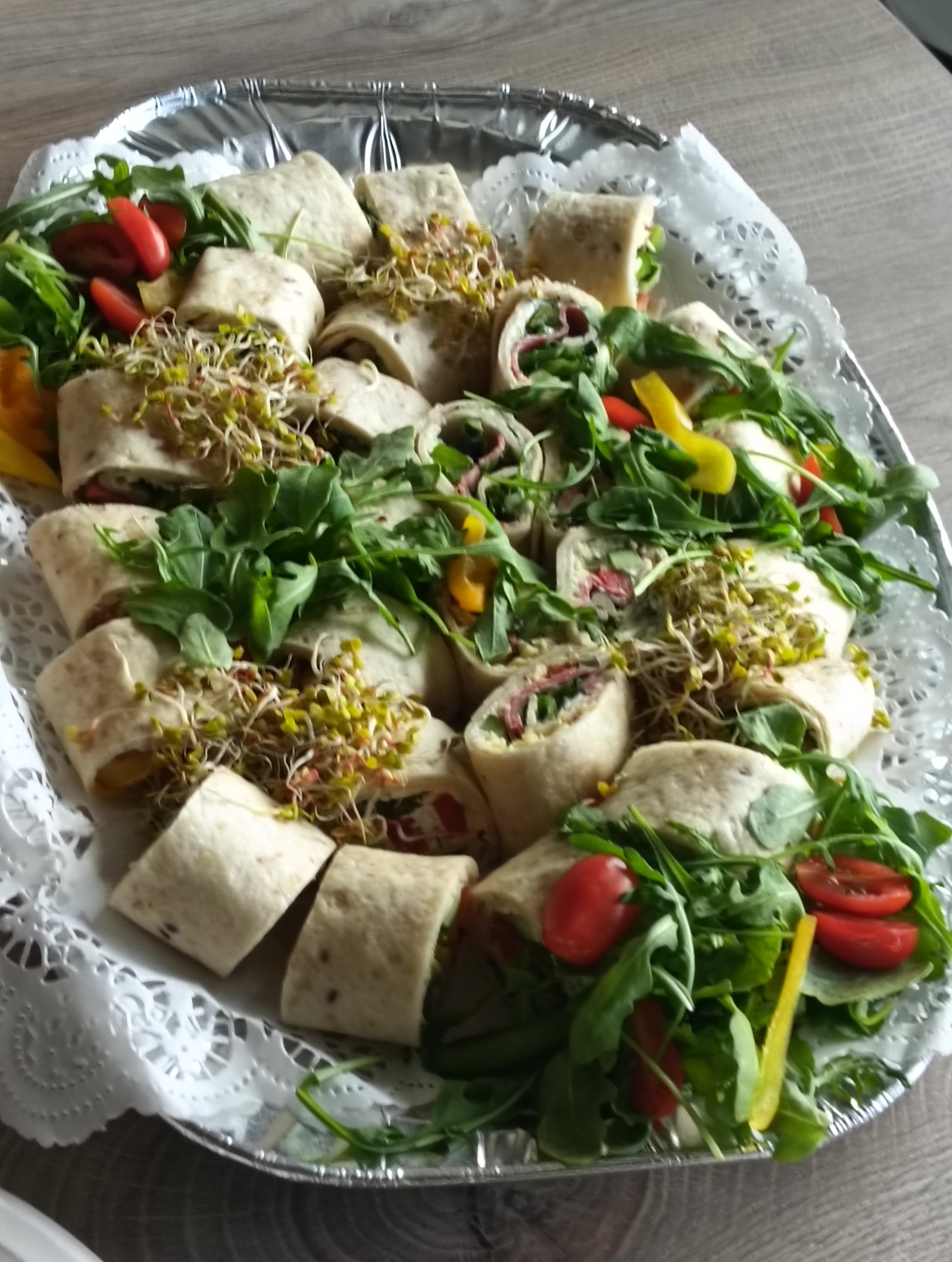 Tortilla wraps z rukolą, kiełkami i pomidorami na srebrnej tacy z koronkową serwetą, gotowe do serwowania na przyjęciu.
