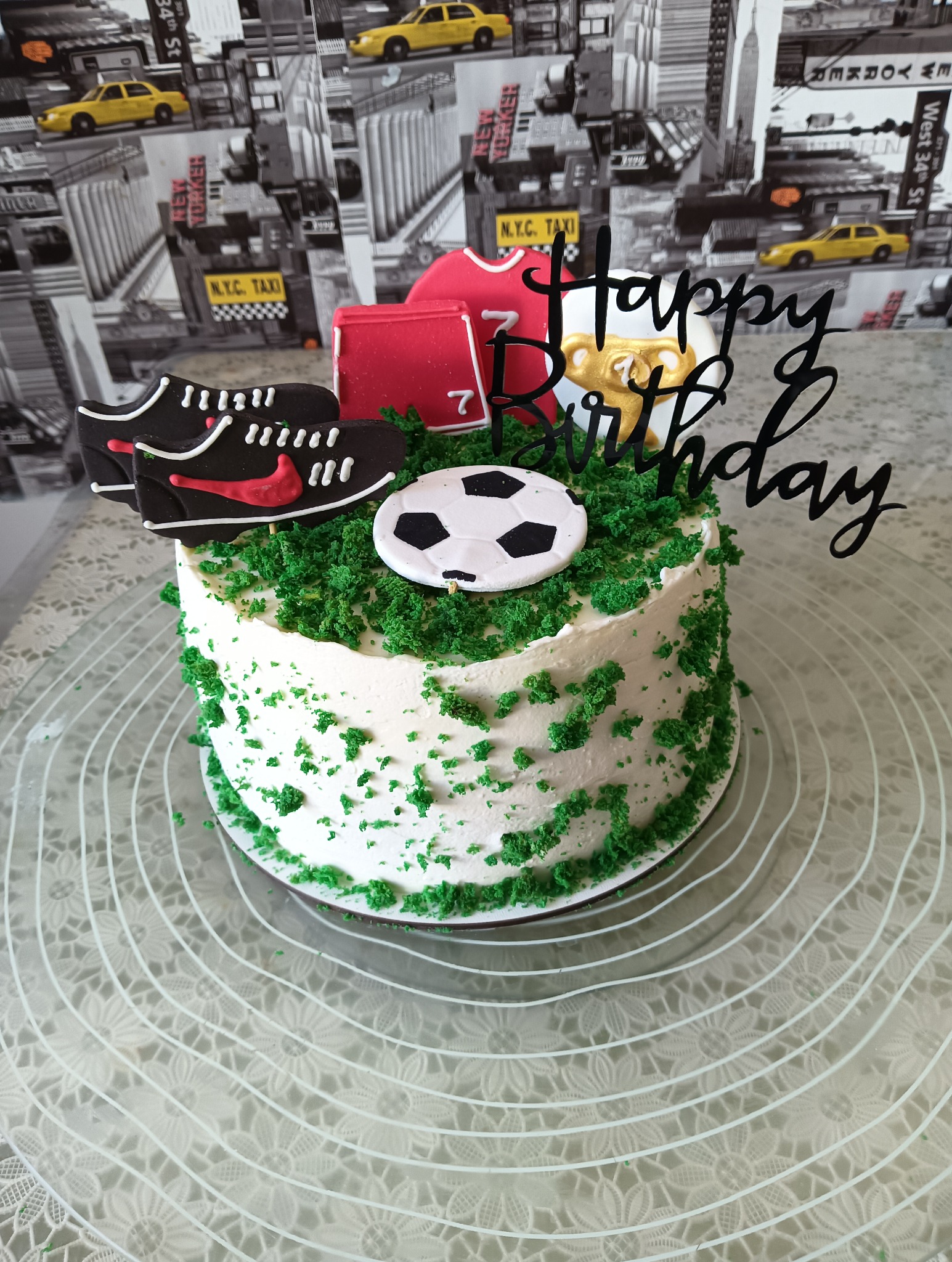 Tort urodzinowy z motywem piłkarskim: zielona posypka imituje trawę, dekoracje z butów, koszulki i piłki. Napis 'Happy Birthday'. Idealny dla fana sportu.