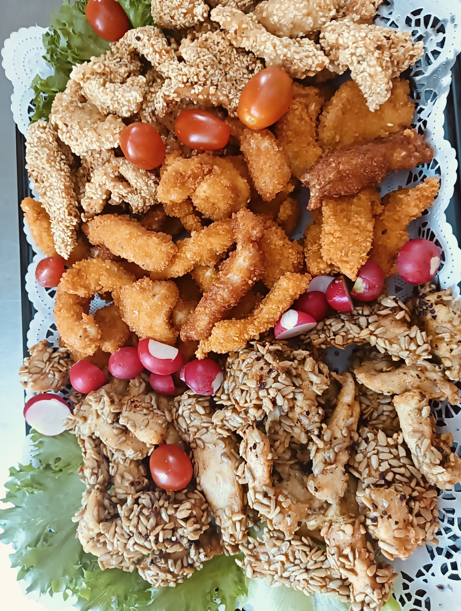 Dekoracyjna taca z różnorodnymi przekąskami: kurczak w sezamie, frytki z kurczaka i warzywa (pomidorki cherry, rzodkiewki). Idealne na przyjęcie.