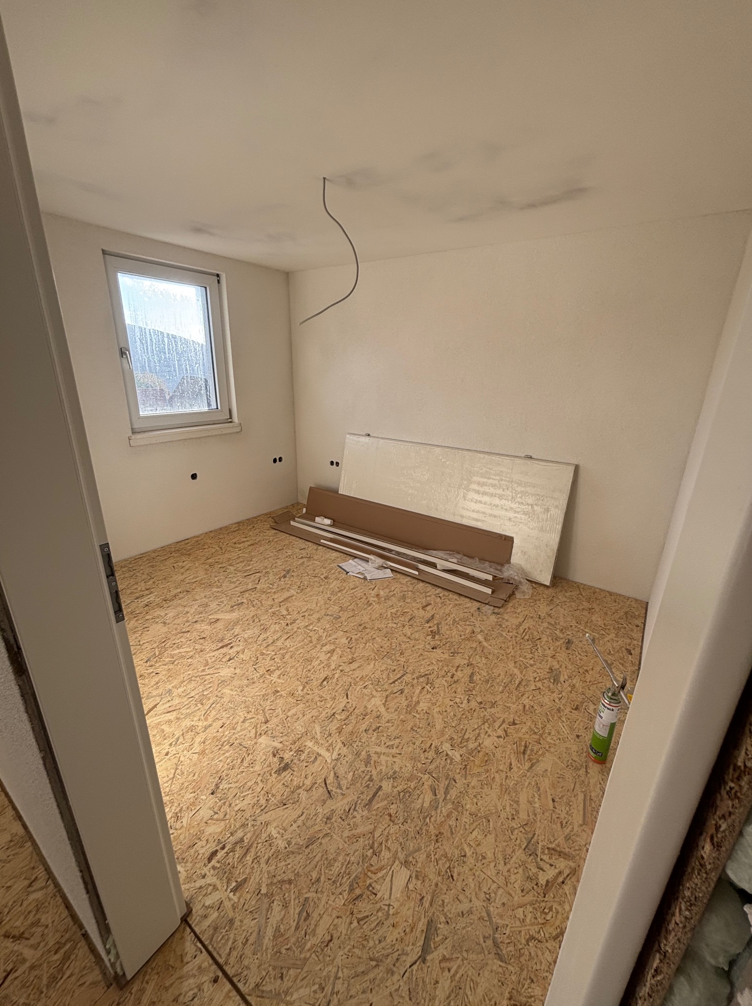 Pokój w trakcie prac wykończeniowych: podłoga z płyt OSB, materiały izolacyjne przy ścianie, widoczne przewody elektryczne. Przygotowanie do dalszych prac.