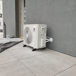 Paweł Maniecki AIRPRO - Zamontowana jednostka zewnętrzna klimatyzacji Gree na balkonie nowoczesnego apartamentowca. Widoczne przewody i osłona na ścianie. Na podłodze zabezpieczenie.