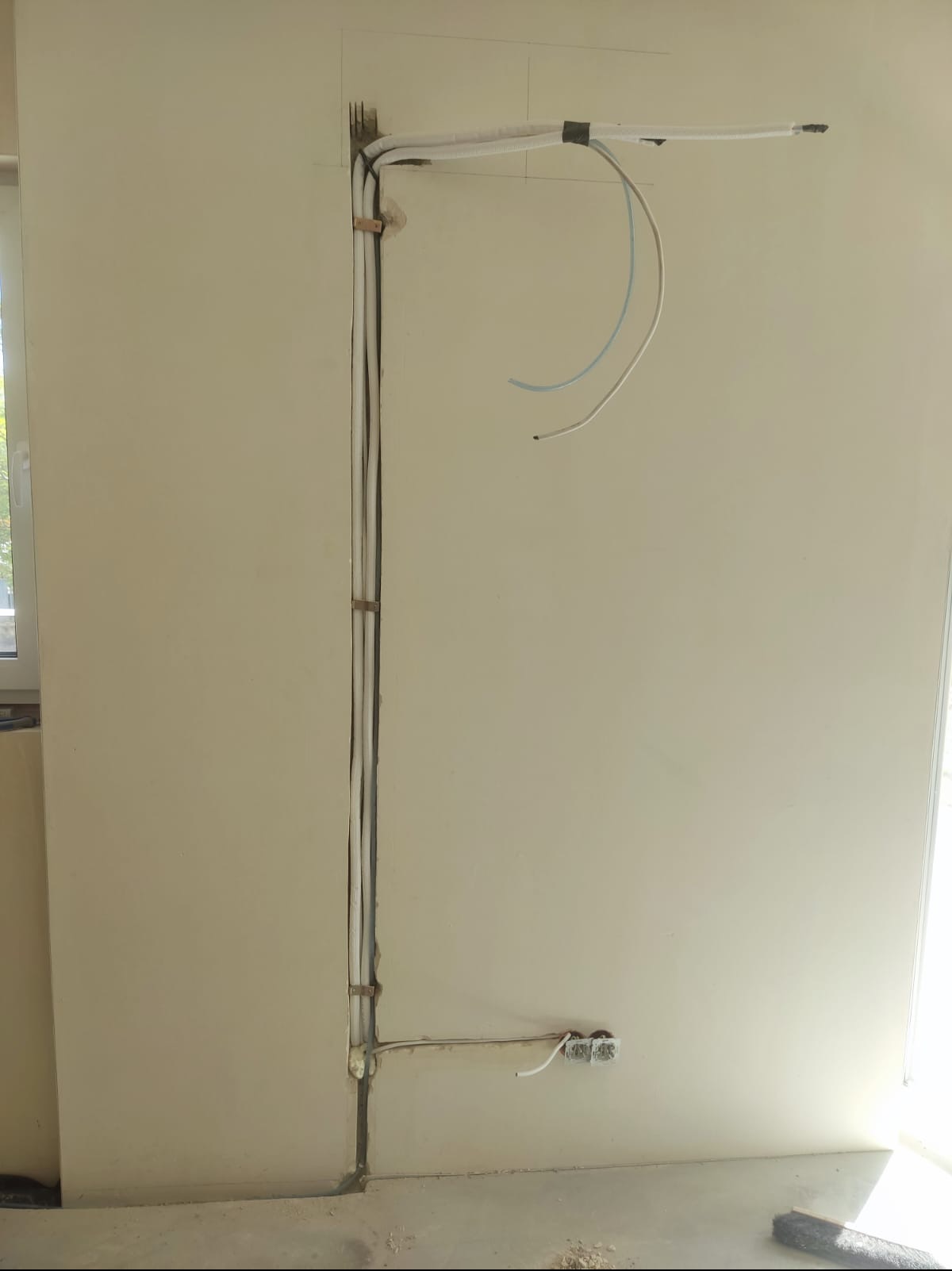 Instalacja przewodów klimatyzacji w ścianie, przygotowanie do montażu klimatyzatora. Widoczne kable i rurki, bruzda w ścianie. Prace instalacyjne w surowym wnętrzu.