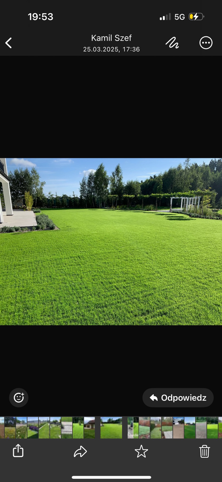 Perfekcyjnie utrzymany trawnik z rolki przed domem, z równo przyciętą trawą i architekturą ogrodową w tle. Widoczne drzewa i pergola.