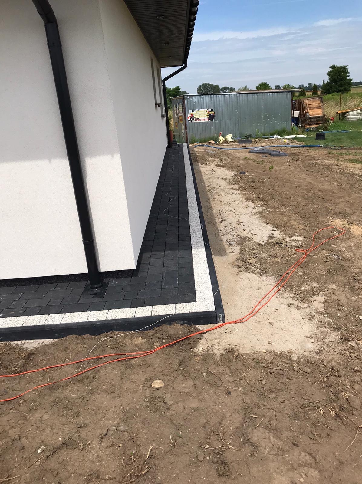 Wykończony chodnik z kostki brukowej w Łodzi, obrzeża z jasnej kostki. Widok na budynek i teren do zagospodarowania.