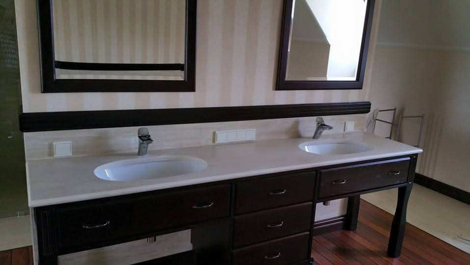 Elegancka łazienka z podwójną umywalką nablatową i ciemnymi szafkami pod blatem. Dwa lustra w ciemnych ramach wiszą nad umywalkami. Paski na ścianie w tle.