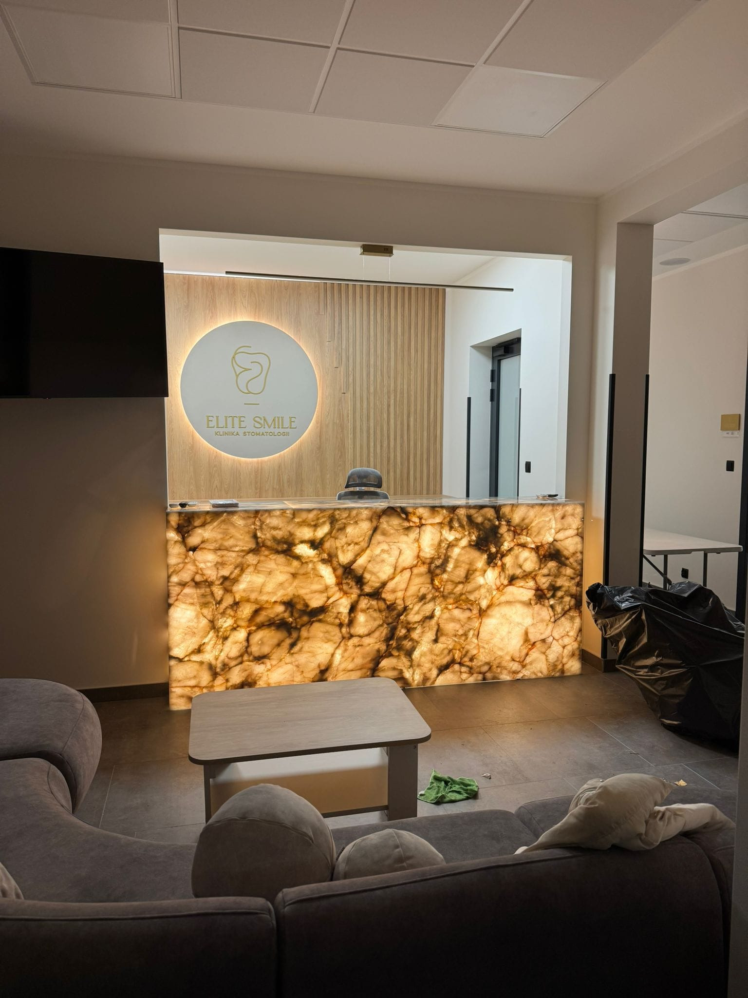 Podświetlany blat recepcyjny z efektem marmuru w nowoczesnej klinice stomatologicznej Elite Smile. Widoczny fragment sofy w poczekalni.