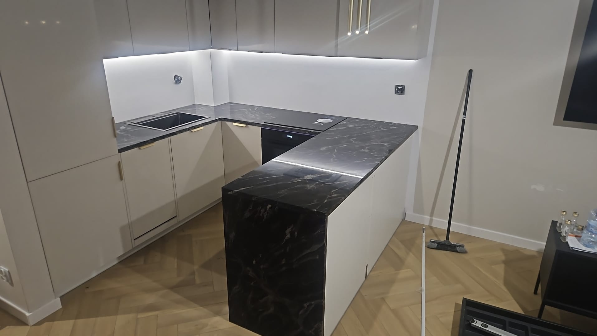 Nowoczesna kuchnia z marmurowym blatem i subtelnym oświetleniem LED. Uwagę przykuwa wzór kamienia i minimalistyczne uchwyty szafek.